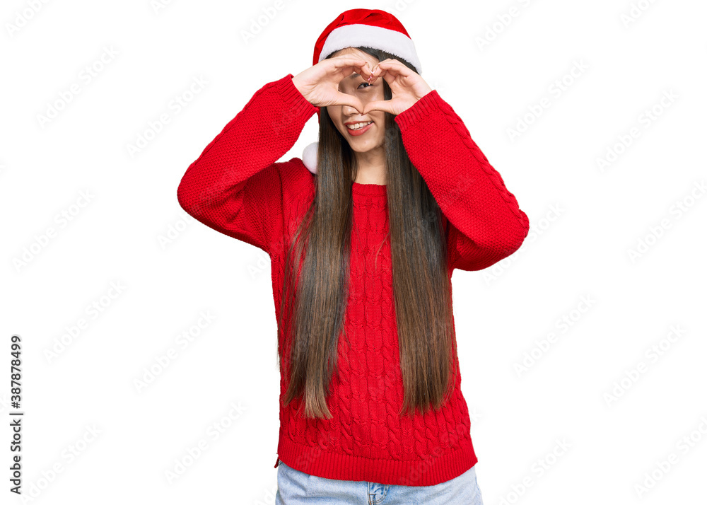 Young chinese woman wearing christmas hat doing heart shape with hand and fingers smiling looking through sign Young chinese woman wearing christmas hat doing heart shape with hand and fingers smiling looking through sign