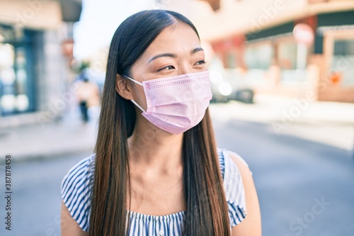 Young chinese woman wearing medical mask walking at street of city.