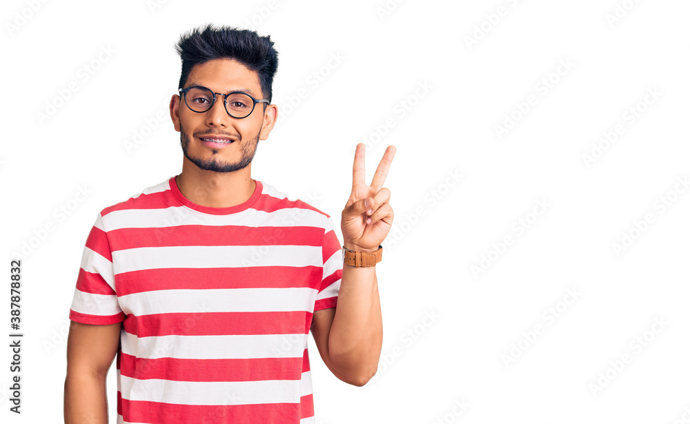 Handsome latin american young man wearing casual clothes and glasses smiling looking to the camera showing fingers doing victory sign. number two. Handsome latin american young man wearing casual clothes and glasses smiling looking to the camera showing fingers doing victory sign. number two.