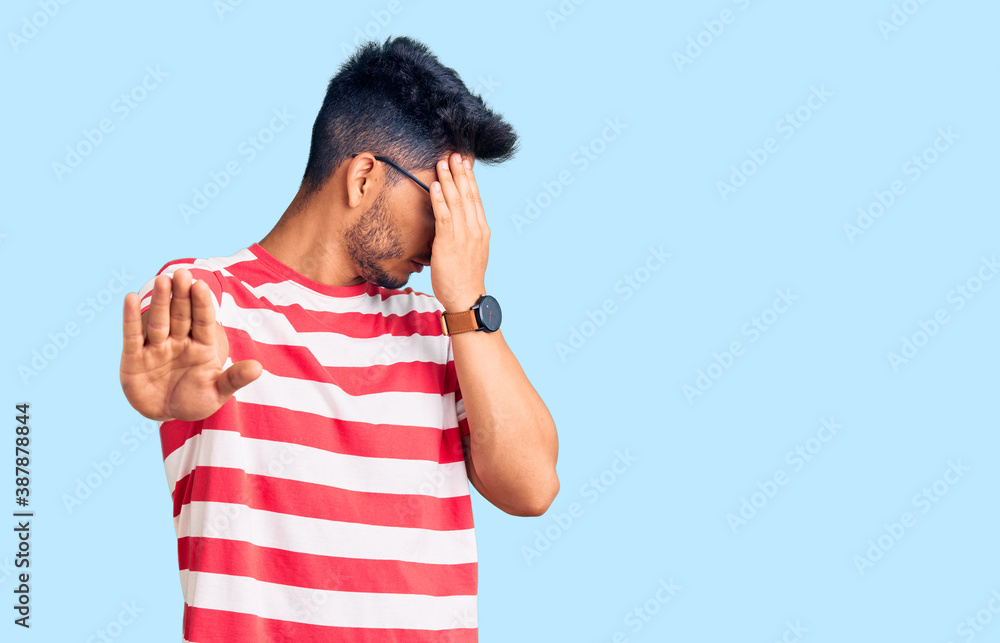 Handsome latin american young man wearing casual clothes and glasses covering eyes with hands and doing stop gesture with sad and fear expression. embarrassed and negative concept. Handsome latin american young man wearing casual clothes and glasses covering eyes with hands and doing stop gesture with sad and fear expression. embarrassed and negative concept.
