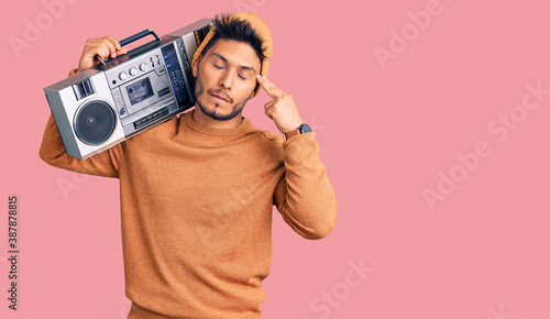 Handsome latin american young man holding boombox, listening to music shooting and killing oneself pointing hand and fingers to head like gun, suicide gesture.