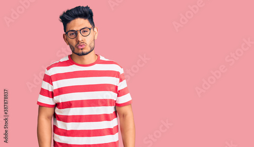 Handsome latin american young man wearing casual clothes and glasses looking at the camera blowing a kiss on air being lovely and sexy. love expression.
