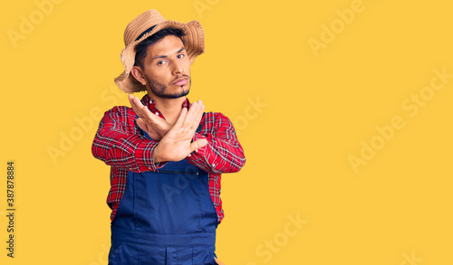 Handsome latin american young man weaing handyman uniform rejection expression crossing arms and palms doing negative sign, angry face