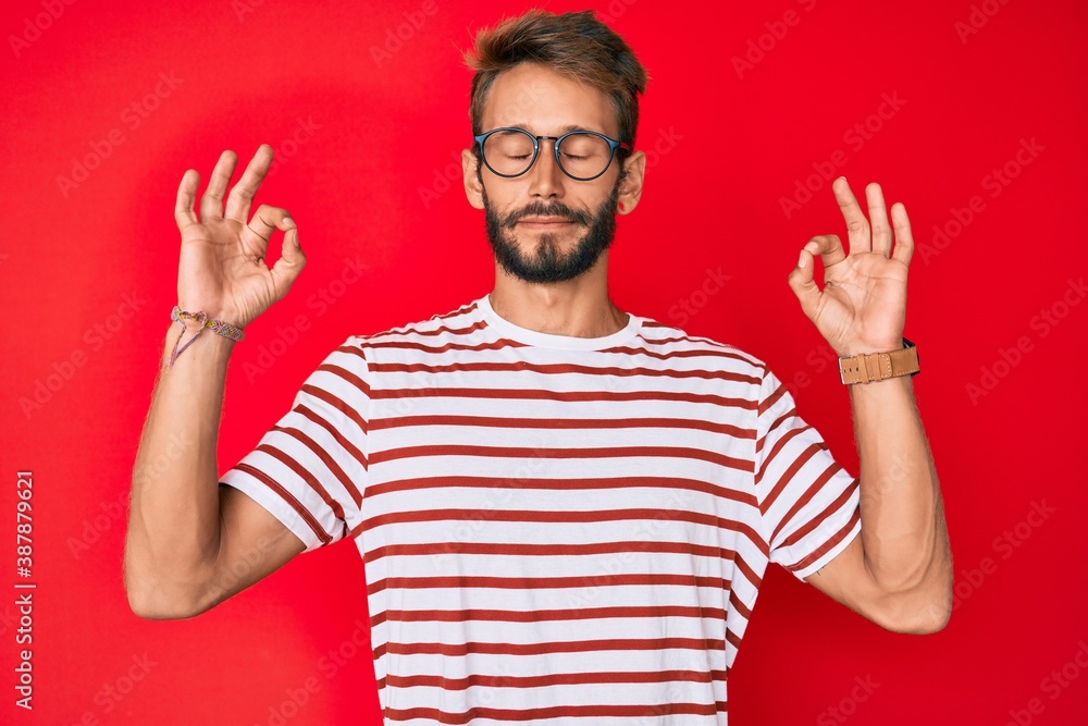 Handsome caucasian man with beard wearing casual clothes and glasses relax and smiling with eyes closed doing meditation gesture with fingers. yoga concept. Handsome caucasian man with beard wearing casual clothes and glasses relax and smiling with eyes closed doing meditation gesture with fingers. yoga concept.