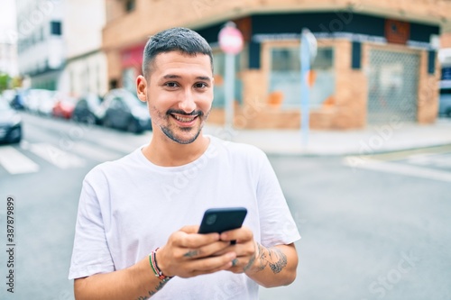 Young hispanic man smiling happy using smartphone at street of city. © Krakenimages.com