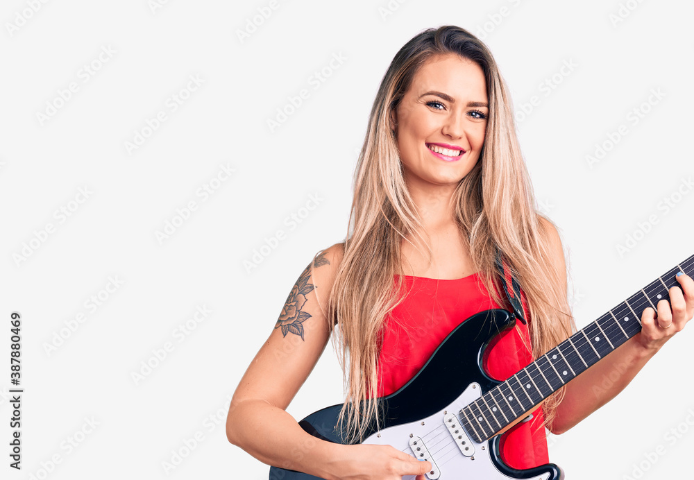 Young beautiful blonde woman playing electric guitar looking positive and happy standing and smiling with a confident smile showing teeth Young beautiful blonde woman playing electric guitar looking positive and happy standing and smiling with a confident smile showing teeth