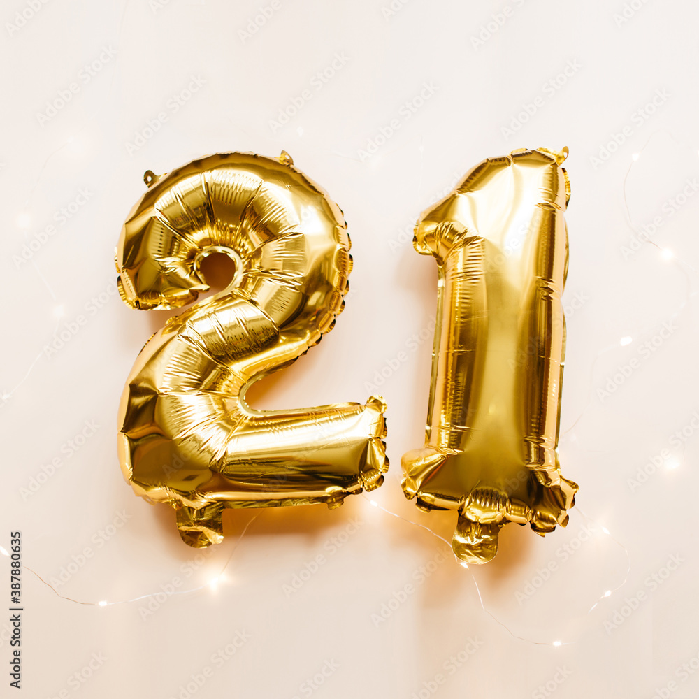 Gold foil balloons number 21 twenty one on beige background. Merry Christmas, happy new year 2021, birthday concept. Party decoration. Flat lay, top view, copy space