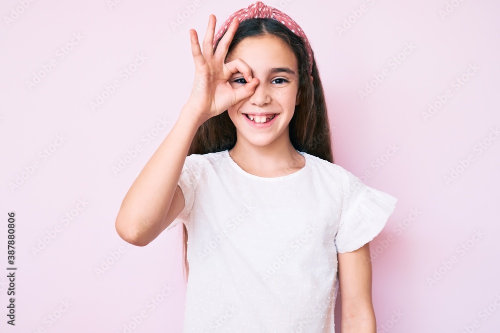 Cute hispanic child girl wearing casual clothes and diadem doing ok gesture with hand smiling, eye looking through fingers with happy face. Cute hispanic child girl wearing casual clothes and diadem doing ok gesture with hand smiling, eye looking through fingers with happy face.