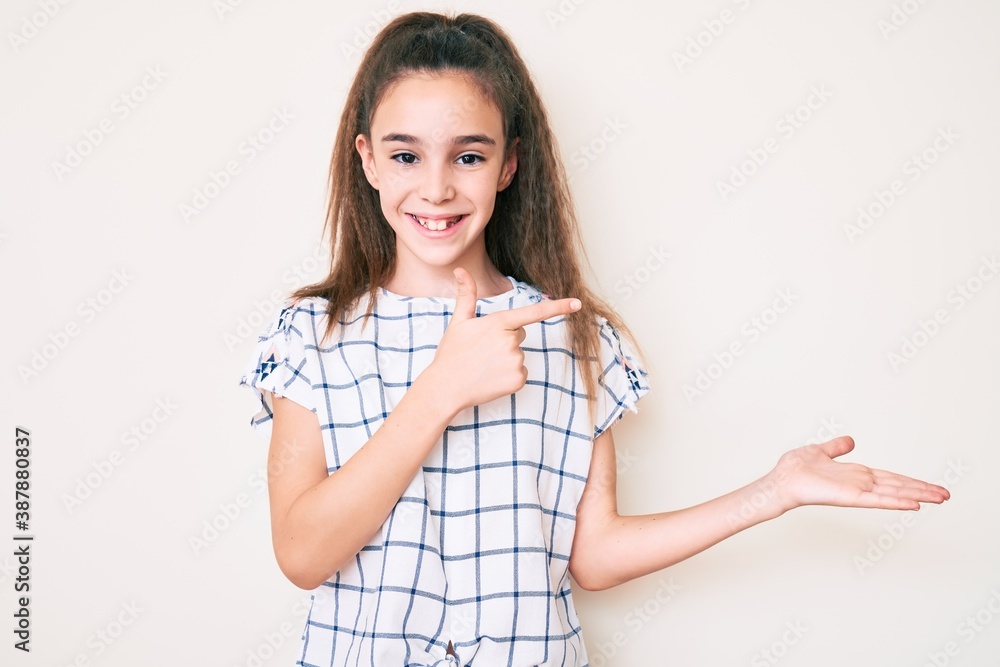 Cute hispanic child girl wearing casual clothes amazed and smiling to the camera while presenting with hand and pointing with finger. Cute hispanic child girl wearing casual clothes amazed and smiling to the camera while presenting with hand and pointing with finger.