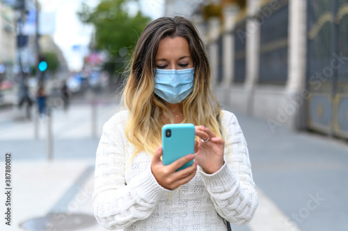 Serious girl with mask checking her phone on street