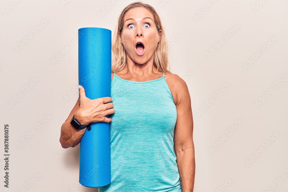Middle age caucasian blonde woman holding yoga mat scared and amazed with open mouth for surprise, disbelief face Middle age caucasian blonde woman holding yoga mat scared and amazed with open mouth for surprise, disbelief face