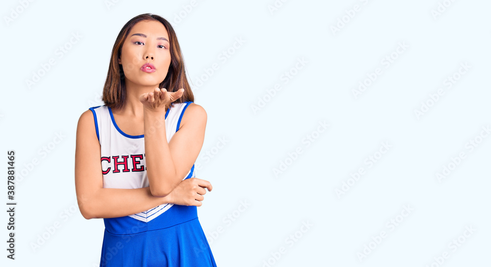 Young beautiful chinese girl wearing cheerleader uniform looking at the camera blowing a kiss with hand on air being lovely and sexy. love expression. Young beautiful chinese girl wearing cheerleader uniform looking at the camera blowing a kiss with hand on air being lovely and sexy. love expression.