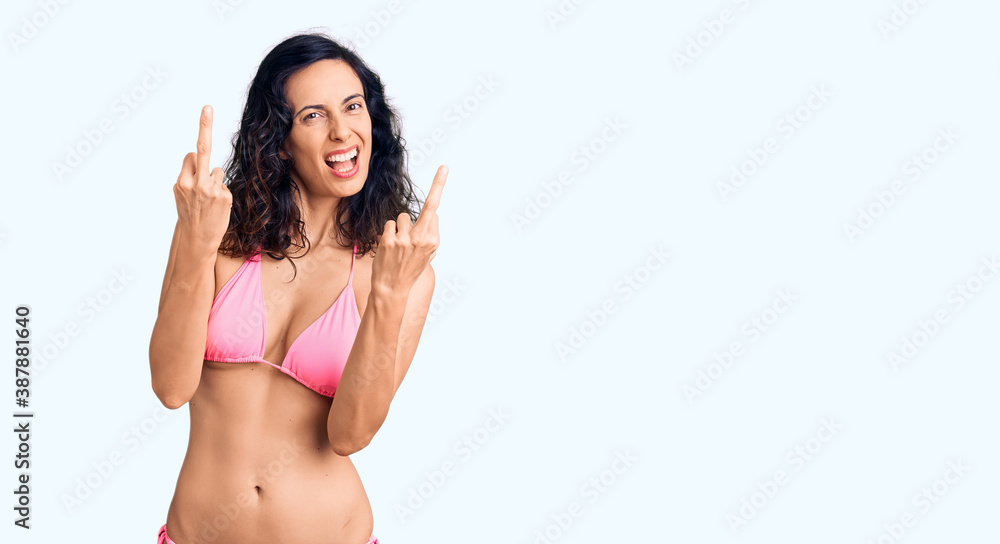 Young beautiful hispanic woman wearing bikini showing middle finger doing fuck you bad expression, provocation and rude attitude. screaming excited Young beautiful hispanic woman wearing bikini showing middle finger doing fuck you bad expression, provocation and rude attitude. screaming excited
