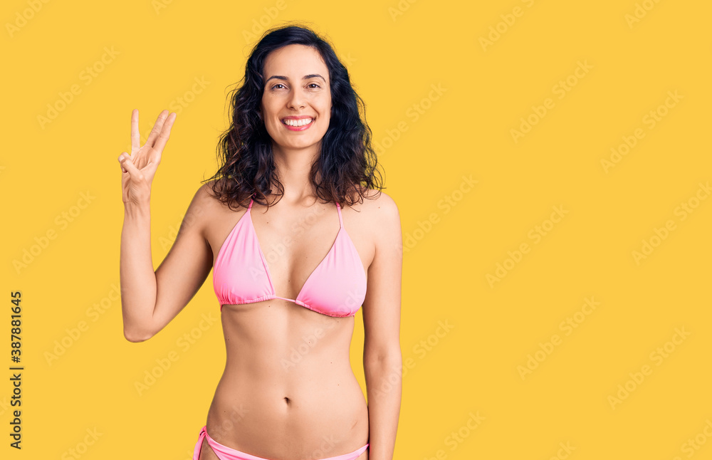 Young beautiful hispanic woman wearing bikini showing and pointing up with fingers number three while smiling confident and happy. Young beautiful hispanic woman wearing bikini showing and pointing up with fingers number three while smiling confident and happy.