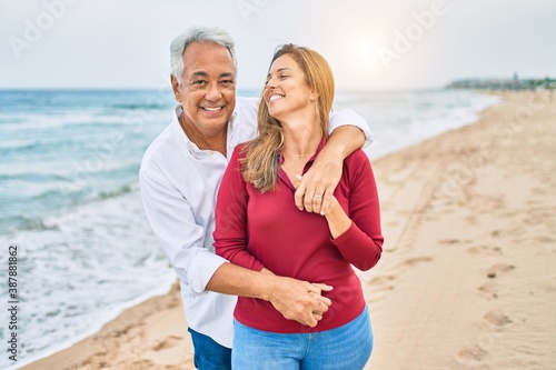 Middle age hispanic couple smiling happy and hugging walking at the beach