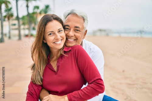 Middle age hispanic couple smiling happy and hugging sitting on the bench. photo
