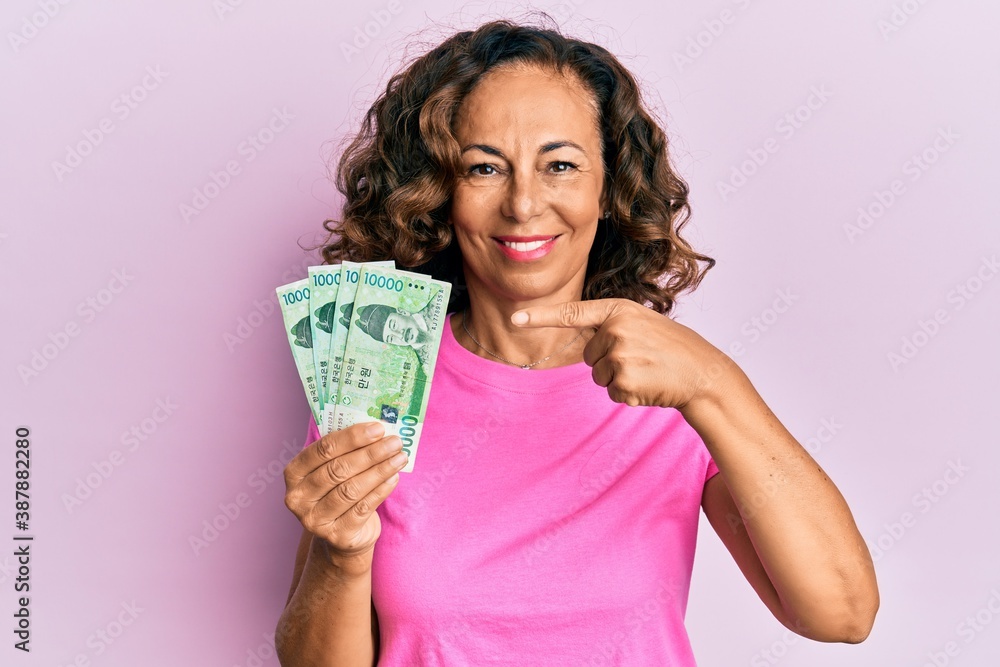 Middle age hispanic woman holding 10000 south korean won banknotes smiling happy pointing with hand and finger Middle age hispanic woman holding 10000 south korean won banknotes smiling happy pointing with hand and finger