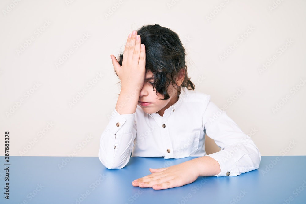 Cute hispanic child wearing casual clothes sitting on the table surprised with hand on head for mistake, remember error. forgot, bad memory concept. Cute hispanic child wearing casual clothes sitting on the table surprised with hand on head for mistake, remember error. forgot, bad memory concept.