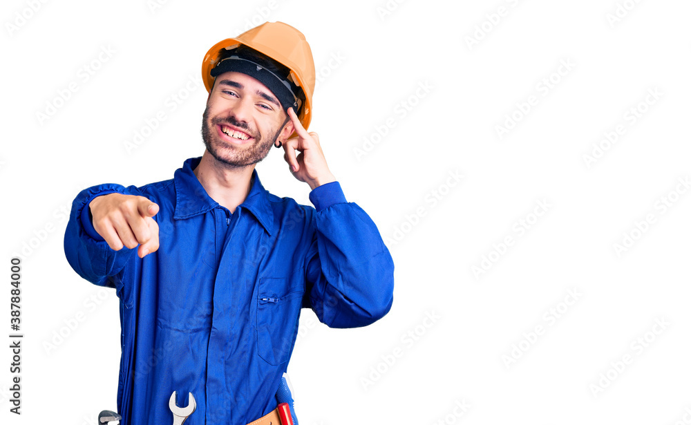 Young hispanic man wearing worker uniform smiling doing talking on the telephone gesture and pointing to you. call me. Young hispanic man wearing worker uniform smiling doing talking on the telephone gesture and pointing to you. call me.