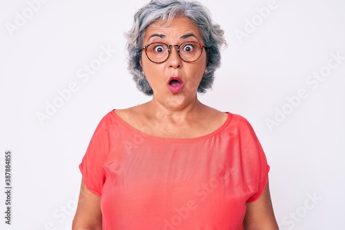 Senior hispanic grey- haired woman wearing casual clothes and glasses afraid and shocked with surprise expression, fear and excited face.