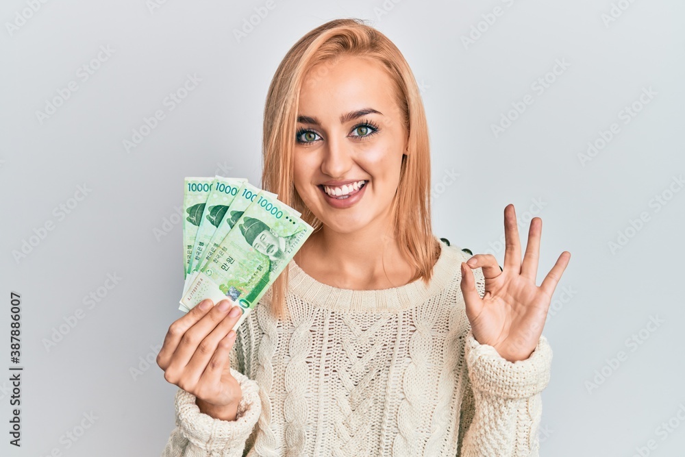 Beautiful caucasian woman holding 10000 south korean won banknotes doing ok sign with fingers, smiling friendly gesturing excellent symbol Beautiful caucasian woman holding 10000 south korean won banknotes doing ok sign with fingers, smiling friendly gesturing excellent symbol