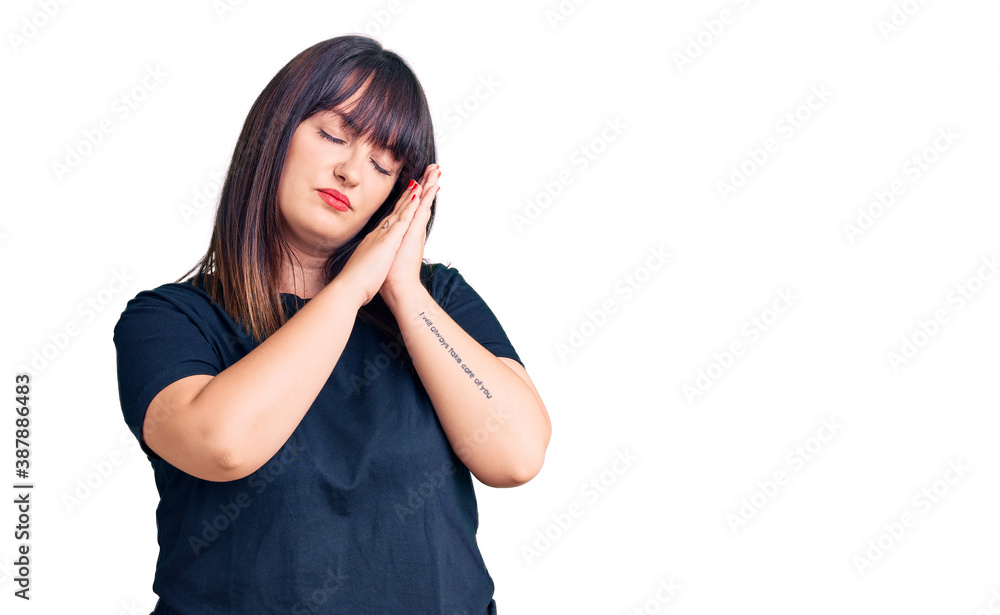 Young plus size woman wearing casual clothes sleeping tired dreaming and posing with hands together while smiling with closed eyes. Young plus size woman wearing casual clothes sleeping tired dreaming and posing with hands together while smiling with closed eyes.