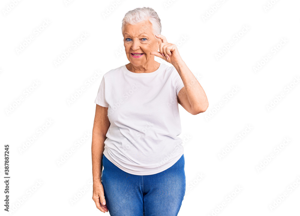 Senior beautiful woman with blue eyes and grey hair wearing casual white tshirt smiling and confident gesturing with hand doing small size sign with fingers looking and the camera. measure concept. Senior beautiful woman with blue eyes and grey hair wearing casual white tshirt smiling and confident gesturing with hand doing small size sign with fingers looking and the camera. measure concept.
