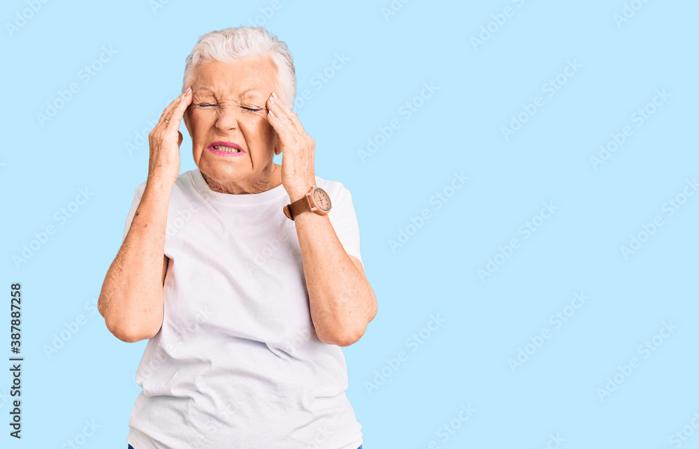 Senior beautiful woman with blue eyes and grey hair wearing casual white tshirt with hand on head, headache because stress. suffering migraine.
