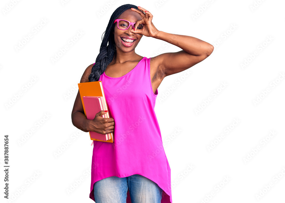 Young african american woman wearing glasses holding book smiling happy doing ok sign with hand on eye looking through fingers Young african american woman wearing glasses holding book smiling happy doing ok sign with hand on eye looking through fingers