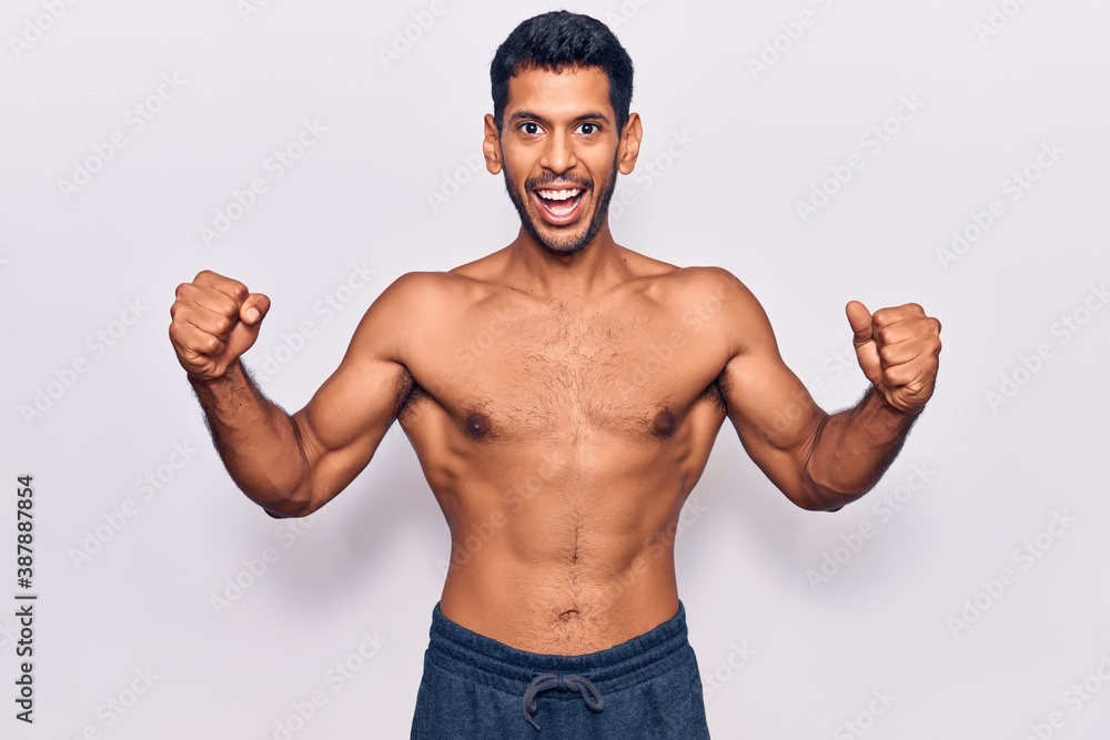 Young latin man standing shirtless celebrating surprised and amazed for success with arms raised and open eyes. winner concept. Young latin man standing shirtless celebrating surprised and amazed for success with arms raised and open eyes. winner concept.