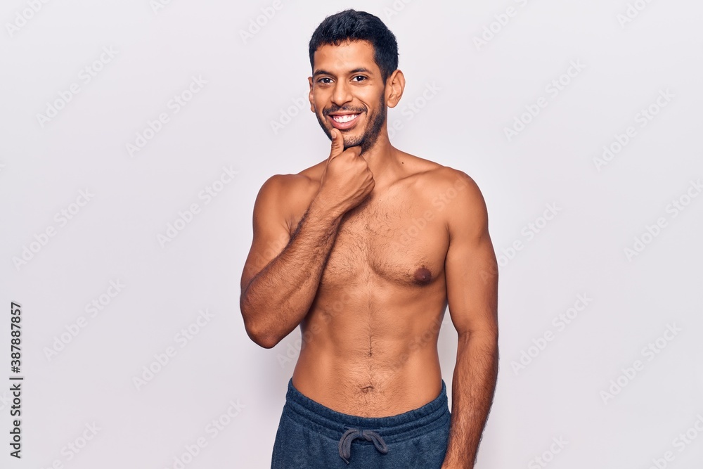 Young latin man standing shirtless looking confident at the camera with smile with crossed arms and hand raised on chin. thinking positive. Young latin man standing shirtless looking confident at the camera with smile with crossed arms and hand raised on chin. thinking positive.