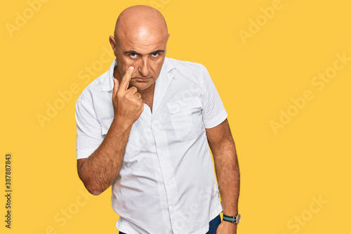 Mature middle east man with mustache wearing casual white shirt pointing to the eye watching you gesture, suspicious expression © Krakenimages.com