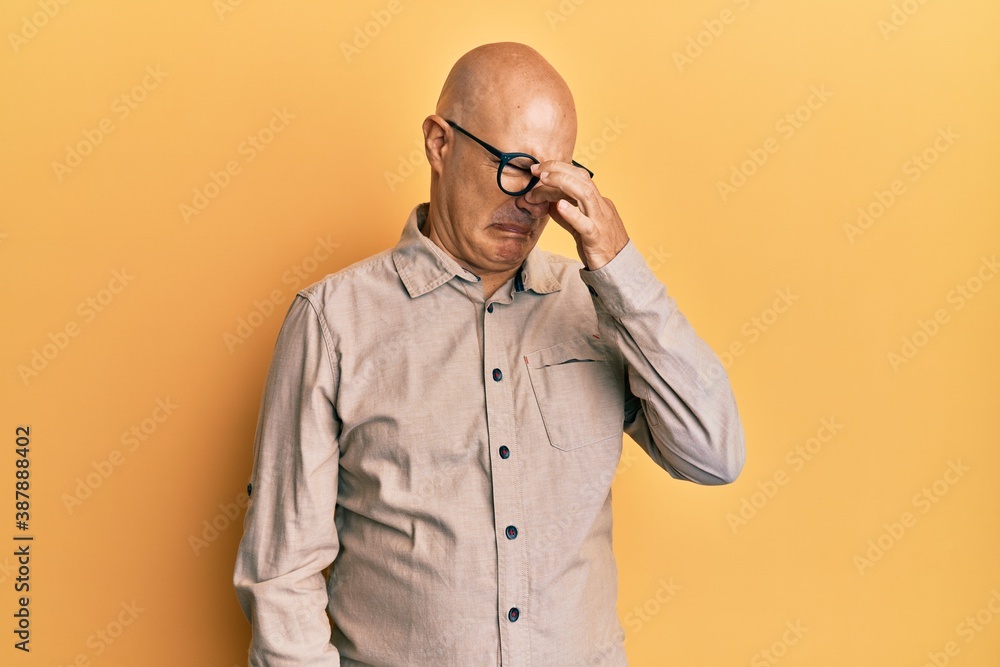 Middle age bald man wearing casual clothes and glasses smelling something stinky and disgusting, intolerable smell, holding breath with fingers on nose. bad smell Middle age bald man wearing casual clothes and glasses smelling something stinky and disgusting, intolerable smell, holding breath with fingers on nose. bad smell