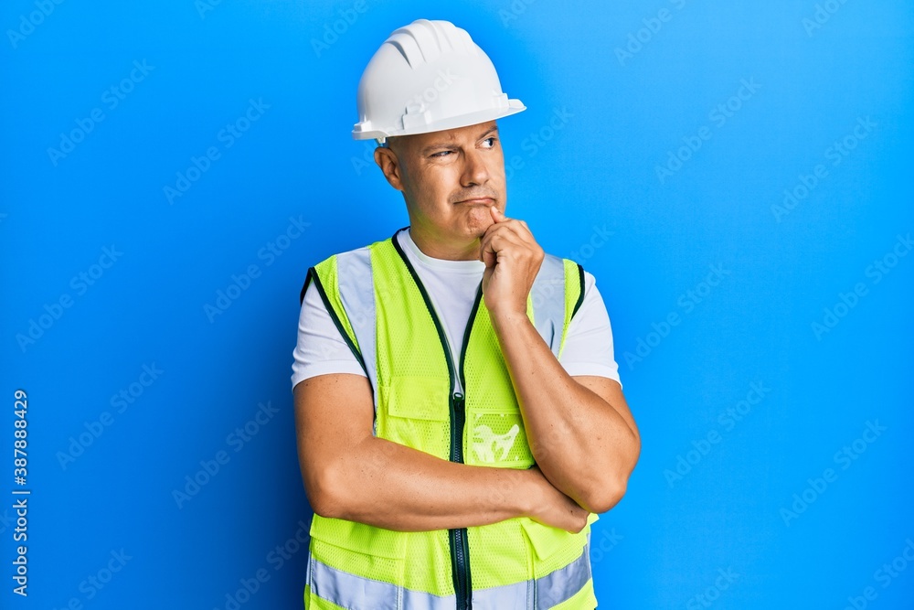 Middle age bald man wearing architect hardhat thinking concentrated about doubt with finger on chin and looking up wondering
