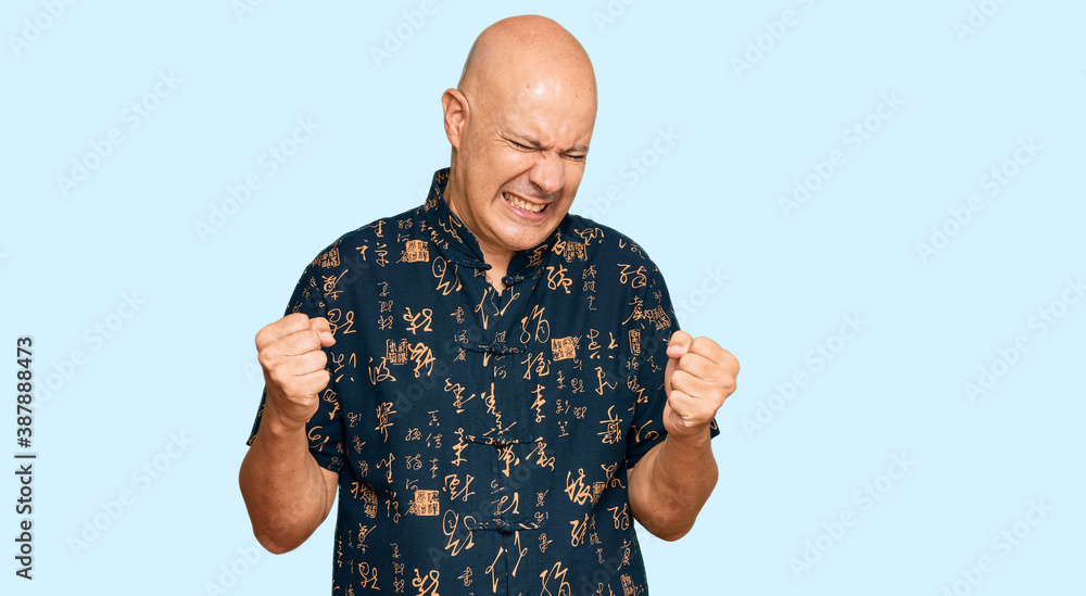 Naklejka premium Middle age bald man wearing casual clothes very happy and excited doing winner gesture with arms raised, smiling and screaming for success. celebration concept.