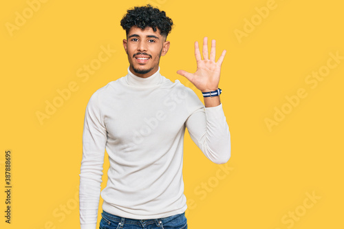 Young arab man wearing casual winter sweater showing and pointing up with fingers number five while smiling confident and happy.