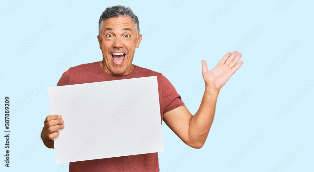 Handsome middle age man holding blank empty banner celebrating victory with happy smile and winner expression with raised hands Handsome middle age man holding blank empty banner celebrating victory with happy smile and winner expression with raised hands