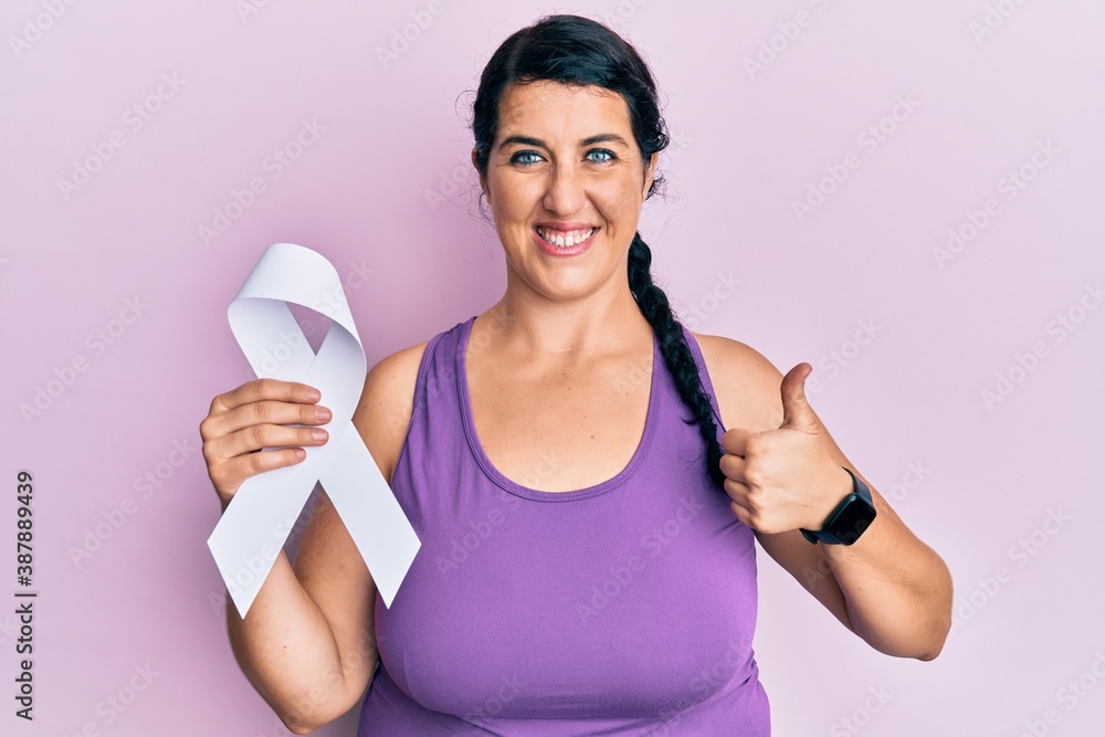 Plus size brunette woman holding white ribbon smiling happy and positive, thumb up doing excellent and approval sign Plus size brunette woman holding white ribbon smiling happy and positive, thumb up doing excellent and approval sign