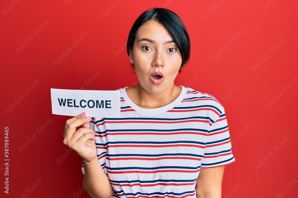 Beautiful young woman with short hair holding welcome paper scared and amazed with open mouth for surprise, disbelief face Beautiful young woman with short hair holding welcome paper scared and amazed with open mouth for surprise, disbelief face