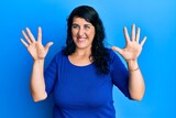 Plus size brunette woman wearing casual blue shirt showing and pointing up with fingers number ten while smiling confident and happy.