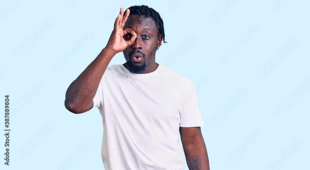 Young african american man with braids wearing casual white tshirt doing ok gesture shocked with surprised face, eye looking through fingers. unbelieving expression. Young african american man with braids wearing casual white tshirt doing ok gesture shocked with surprised face, eye looking through fingers. unbelieving expression.