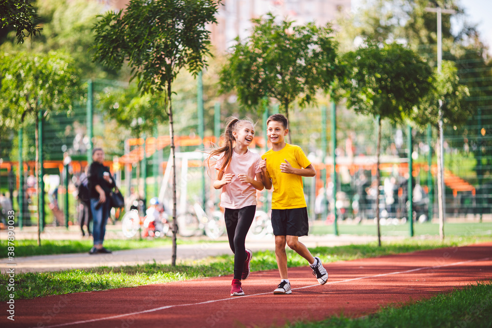 Sports and fitness in adolescence. Caucasian twins boy and girl run on the jogging track in the city park. Two children brother and sister for 10 years running on a rubberized outdoor treadmill