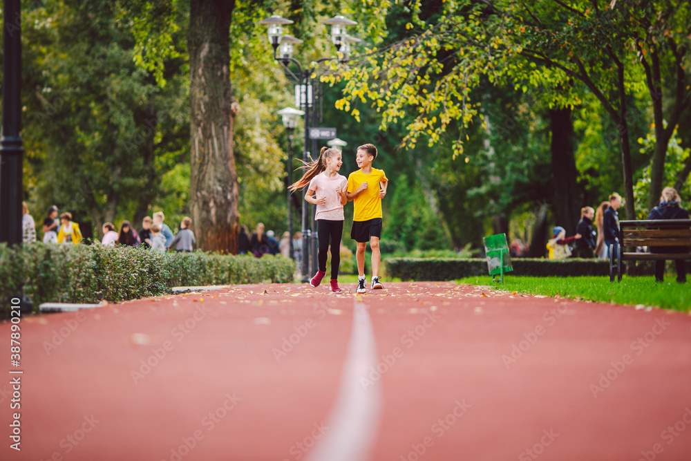 Sports and fitness in adolescence. Caucasian twins boy and girl run on the jogging track in the city park. Two children brother and sister for 10 years running on a rubberized outdoor treadmill