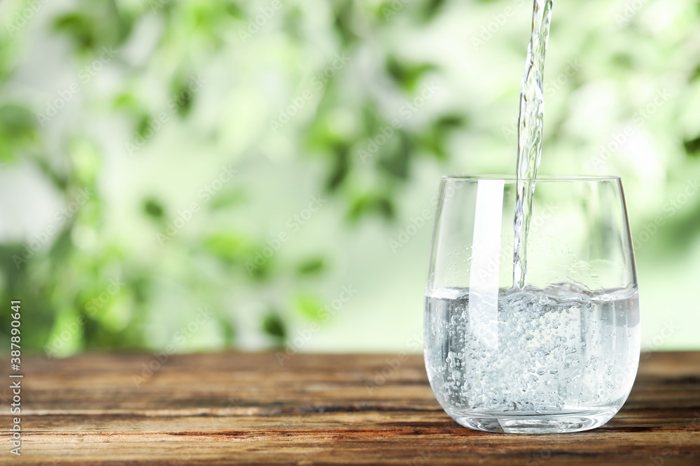 Pouring water into glass on wooden table outdoors, space for text. Refreshing drink Pouring water into glass on wooden table outdoors, space for text. Refreshing drink