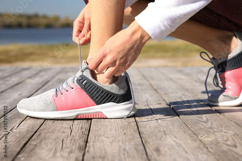 Sporty woman tying shoelaces outdoors on sunny morning, closeup