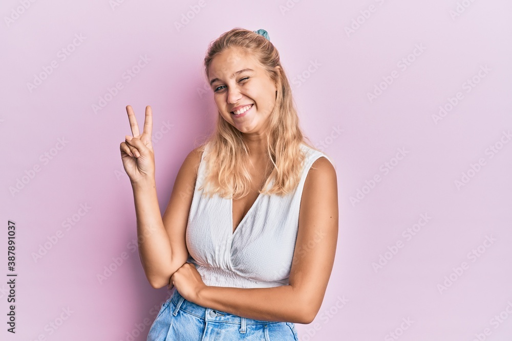 Young blonde girl wearing casual clothes smiling with happy face winking at the camera doing victory sign. number two. Young blonde girl wearing casual clothes smiling with happy face winking at the camera doing victory sign. number two.