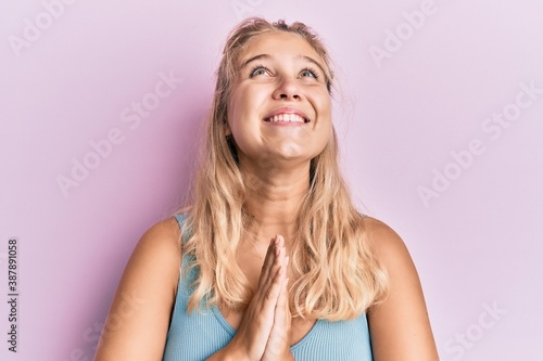 Young blonde girl wearing casual clothes begging and praying with hands together with hope expression on face very emotional and worried. begging.