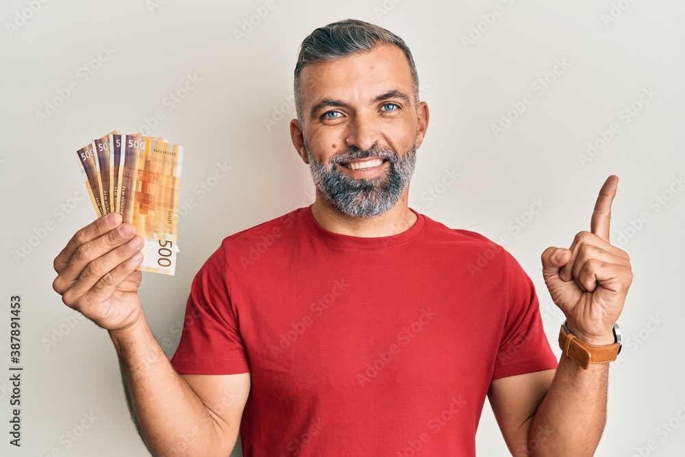 Middle age handsome man holding 500 norwegian krone banknotes smiling happy pointing with hand and finger to the side Middle age handsome man holding 500 norwegian krone banknotes smiling happy pointing with hand and finger to the side