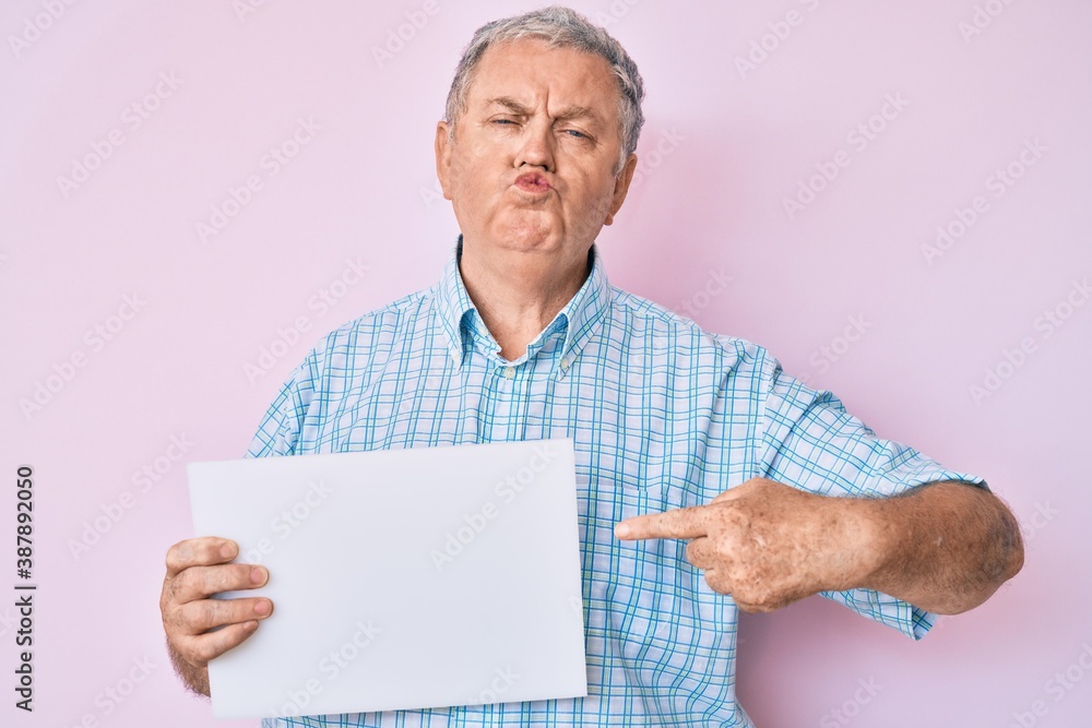 Senior grey-haired man holding blank empty banner looking at the camera blowing a kiss being lovely and sexy. love expression. Senior grey-haired man holding blank empty banner looking at the camera blowing a kiss being lovely and sexy. love expression.
