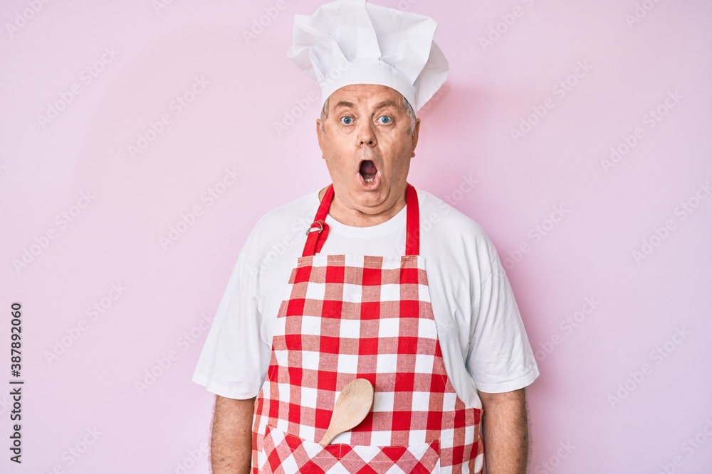 Senior grey-haired man wearing professional baker apron afraid and shocked with surprise expression, fear and excited face. Senior grey-haired man wearing professional baker apron afraid and shocked with surprise expression, fear and excited face.